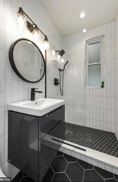 A modern bathroom featuring black tile flooring, chrome fixtures, white subway tile walls, and wood cabinetry.