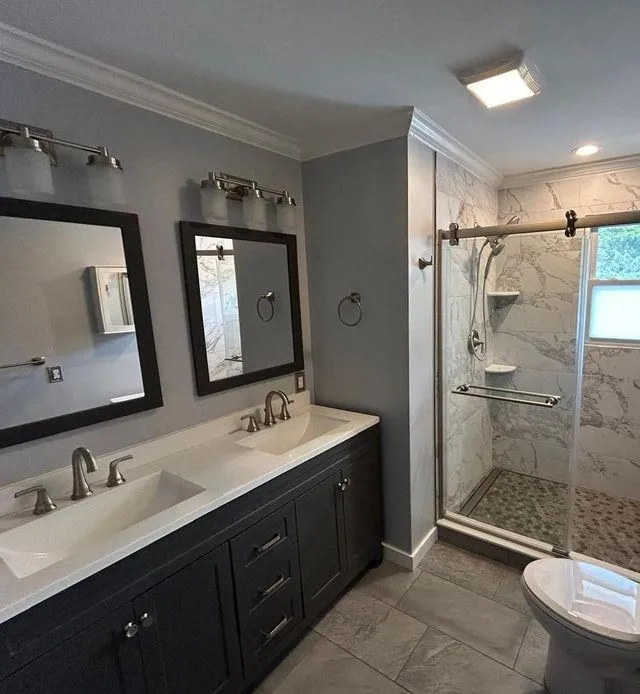 Modern bathroom featuring marble walls, double sink vanity, glass-enclosed shower, and elegant fixtures.