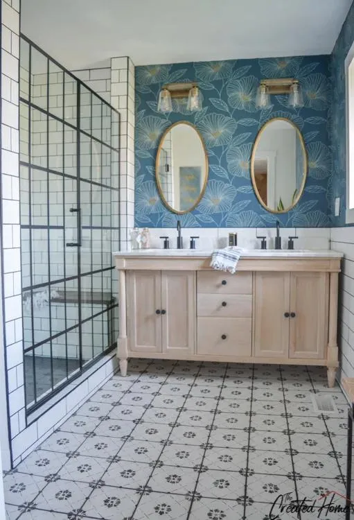 A modern bathroom features a large mirror over a floating vanity with tiled floors and walls, accented by metal fixtures and wooden cabinetry, with a blue polka dot framed wallpaper.