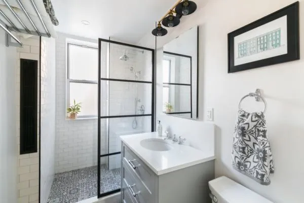 A modern bathroom featuring a floating vanity with white tiles and black metal framing.