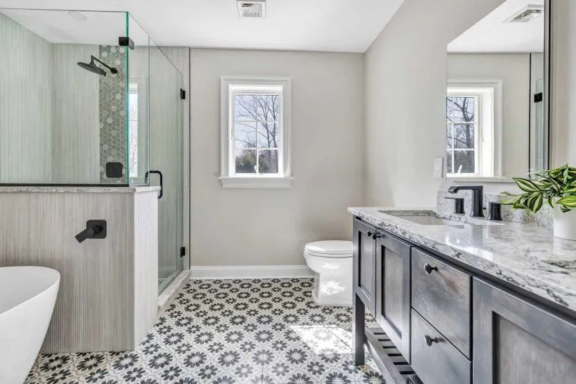 A modern bathroom featuring marble countertops, wooden cabinetry, and a large glass shower enclosure with white ceramic tiles in a neutral color scheme.