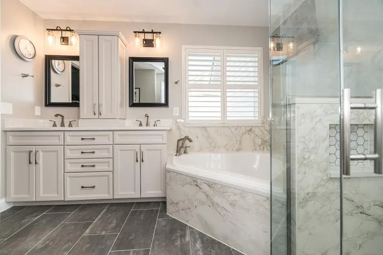 A luxurious, modern bathroom features marble countertops, white subway tiles, dark brown cabinets, and a glass shower enclosure.